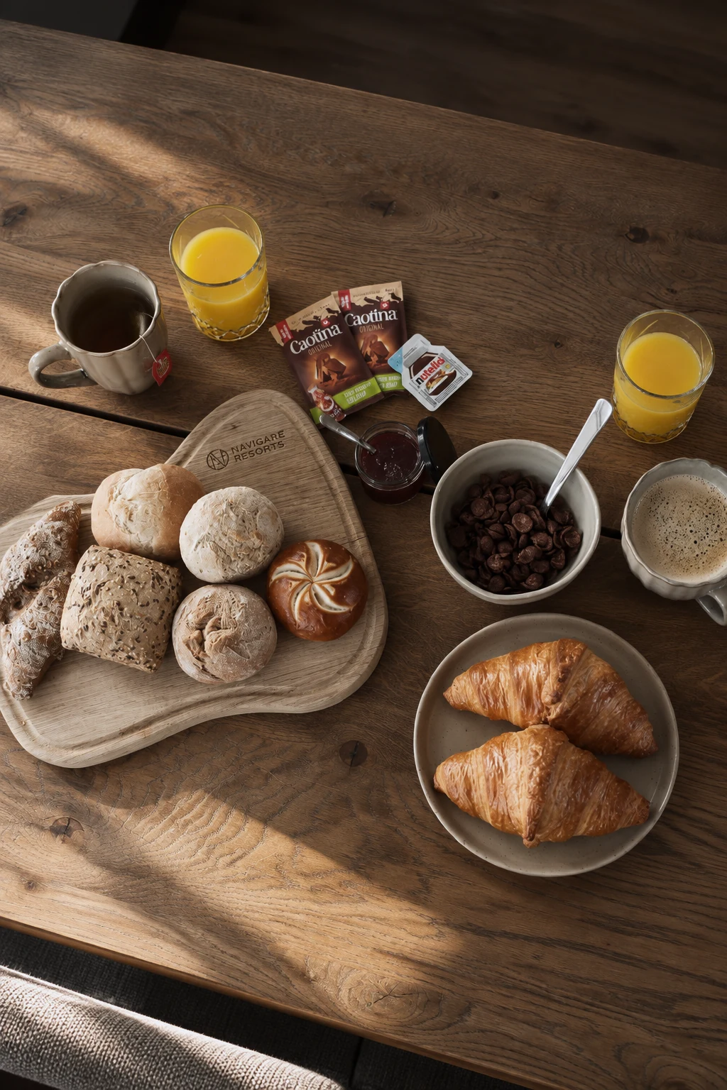 Breakfast at Navigare Resorts with fresh bread, croissants, cereal, orange juice and hot drinks on a wooden table.